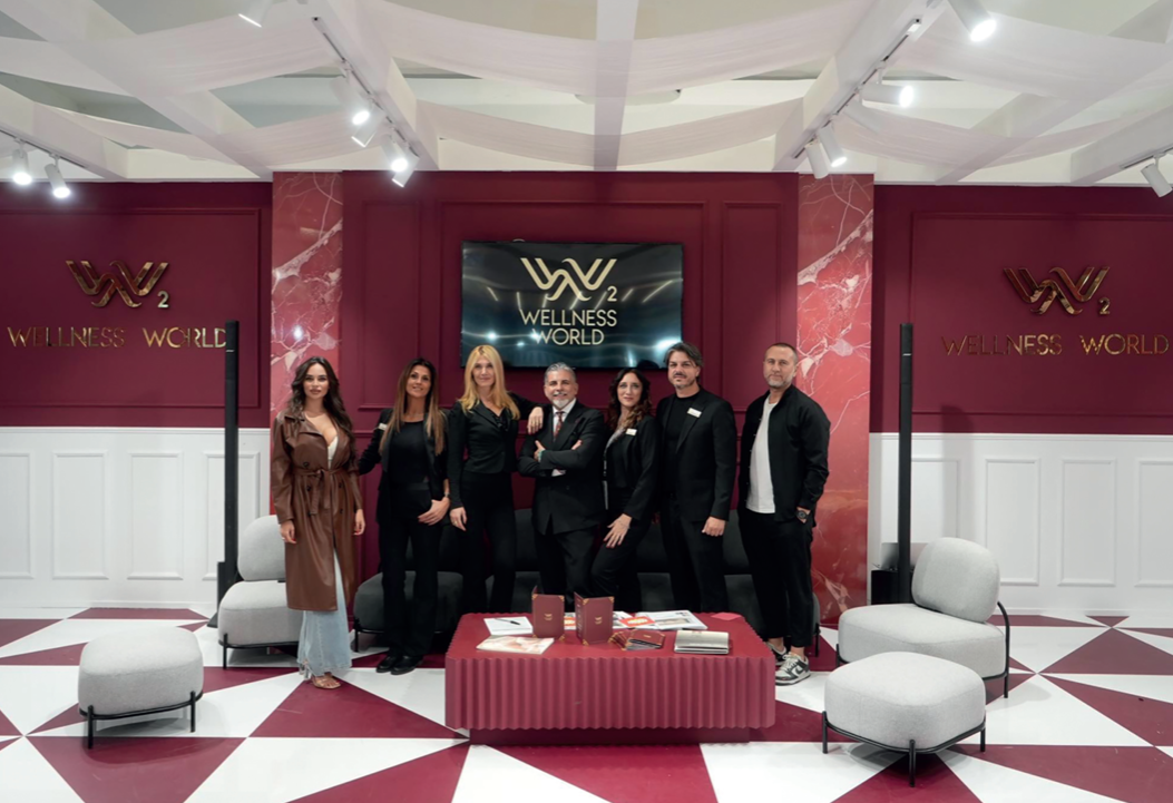 Il team Wellness World allo stand con logo dorato su parete bordeaux